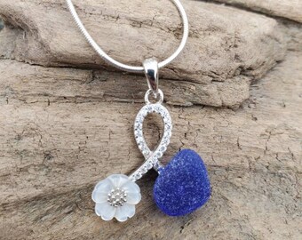 May include: A silver necklace with a blue heart and a white flower pendant. The pendant is set with clear stones and the chain is a snake chain.