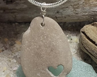May include: A silver chain necklace with a pendant made from a light brown stone with a carved heart shape. The heart is filled with a light green stone.