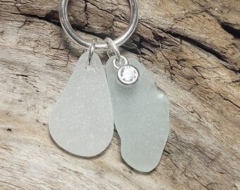 May include: A silver chain necklace with a silver ring and two white sea glass charms. One charm has a small clear rhinestone.