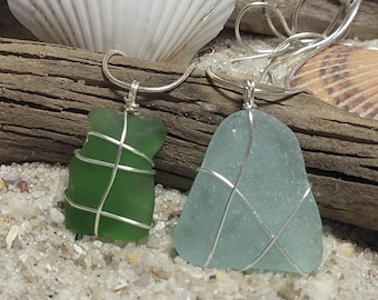 May include: Two sea glass necklaces with silver wire wrapped around the glass. The sea glass is green and blue.