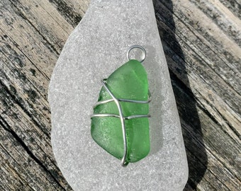 May include: A green sea glass pendant wrapped in silver wire. The pendant is sitting on a white sea glass rock.