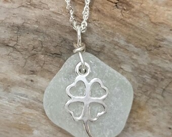 May include: A silver necklace with a four-leaf clover charm attached to a white sea glass pendant.