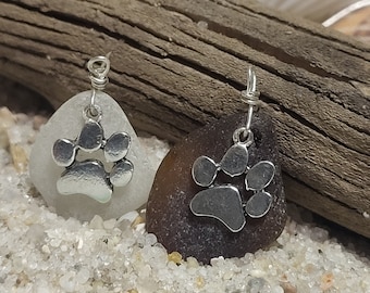 May include: Two sea glass earrings with silver paw print charms. The sea glass is white and brown.