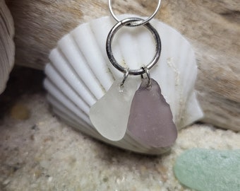 May include: A silver chain necklace with a silver ring charm. The ring charm has two sea glass pieces attached to it, one white and one light purple.