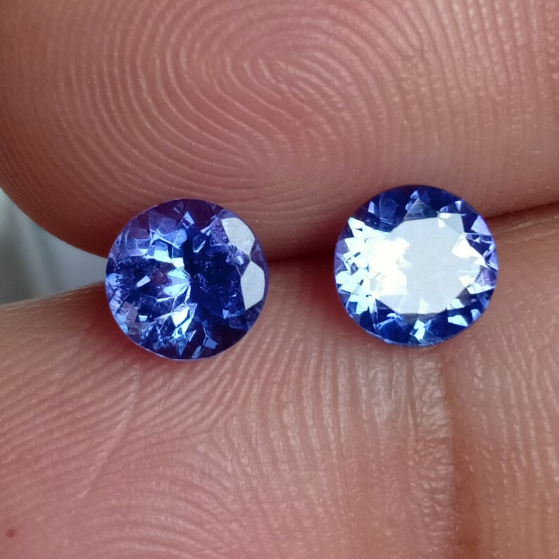 May include: Two round, faceted, blue gemstones. The gemstones are set in a bezel setting and have a high polish.