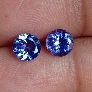 May include: Two round, faceted, blue gemstones. The gemstones are set in a clear, transparent material.