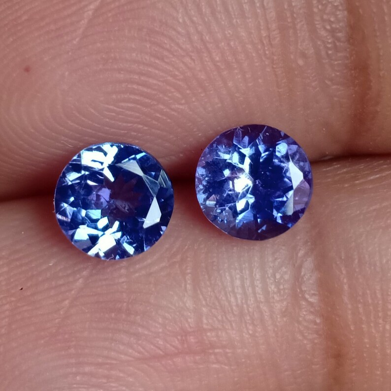May include: Two round, faceted, blue gemstones. The gemstones are set in a clear, transparent material.