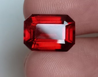 May include: A deep red gemstone with a rectangular emerald cut.