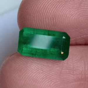 Puede incluir: Una gema de esmeralda verde vibrante, cortada en forma rectangular con un acabado pulido.