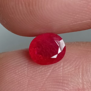 May include: A bright red oval-shaped gemstone with a faceted cut.