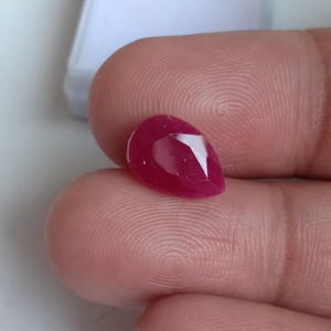 May include: A pear-shaped ruby gemstone with a deep red colour.