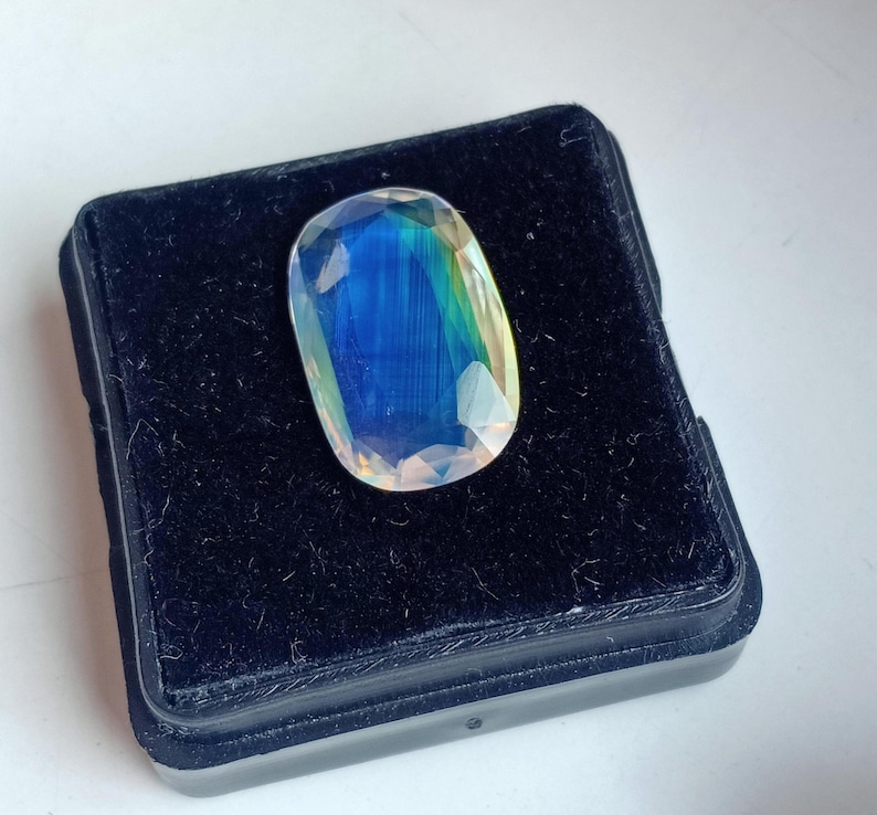 May include: A large, oval-shaped, iridescent gemstone with a blue, green, and yellow color scheme. The gemstone is displayed in a black velvet box.