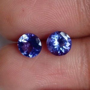 May include: Two oval-shaped, faceted, blue gemstones. The gemstones are set in a clear, transparent material.