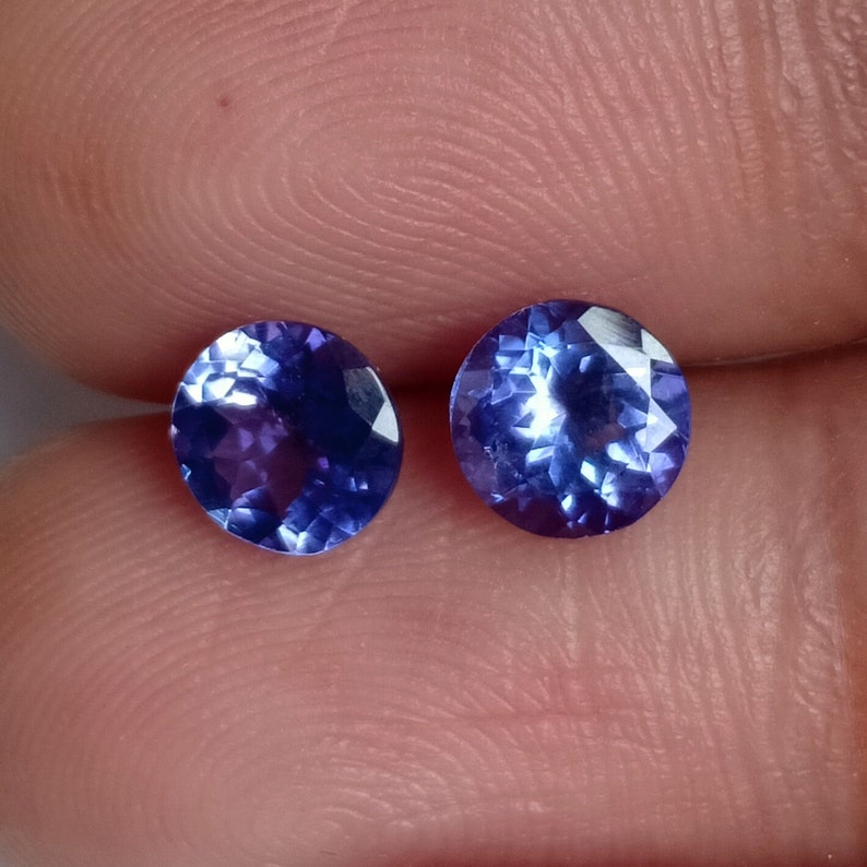 May include: Two oval-shaped, faceted, blue gemstones. The gemstones are set in a clear, transparent material.