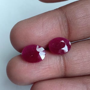Puede incluir: Dos piedras preciosas de rubí de forma ovalada y facetadas. Los rubíes son de color rojo intenso y tienen un alto pulido.