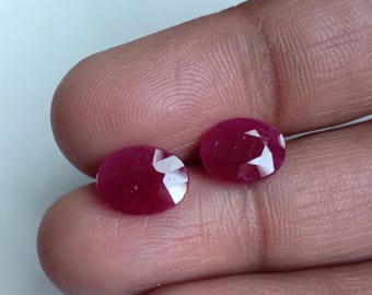 Puede incluir: Dos piedras preciosas de rubí de forma ovalada y facetadas. Los rubíes son de color rojo intenso y tienen un alto pulido.