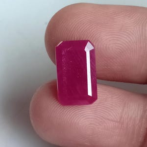 Puede incluir: Una gema rosa vibrante con un corte esmeralda rectangular. La gema está facetada y tiene un alto pulido.