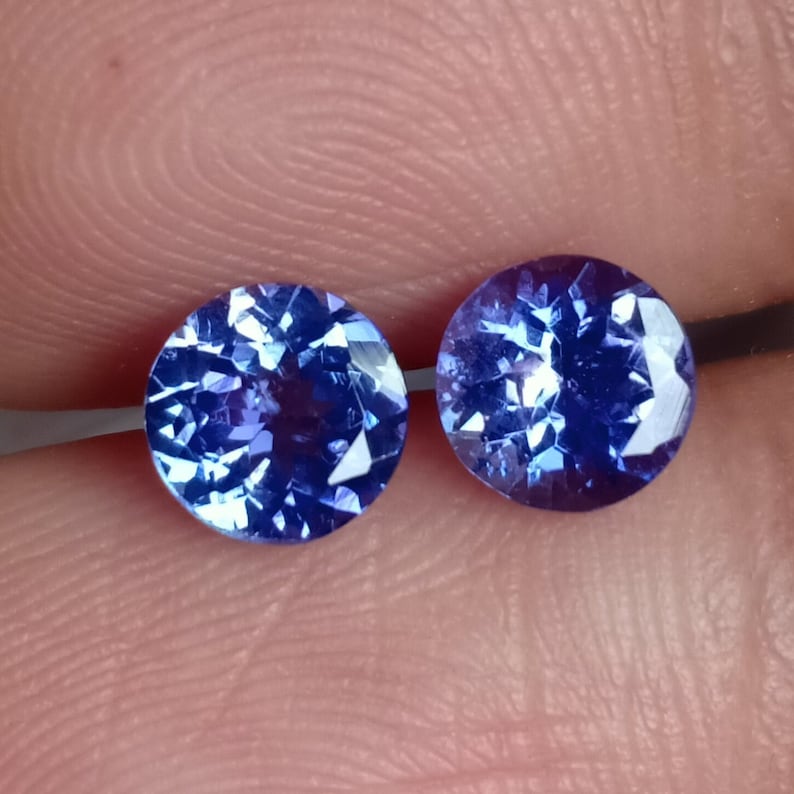 May include: Two round, blue gemstones with a faceted cut. The gemstones are set in a clear, round setting.