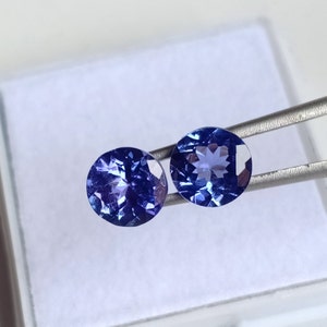 May include: Two round, blue gemstones with a faceted cut. The gemstones are set in a silver tone setting.
