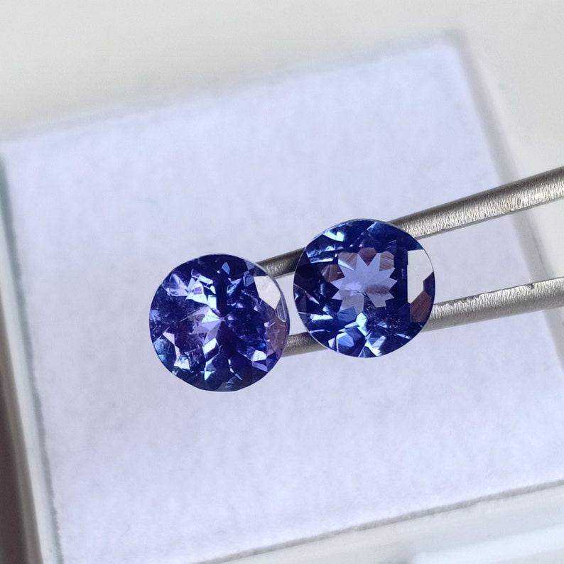 May include: Two round, blue gemstones with a faceted cut. The gemstones are set in a silver tone setting.