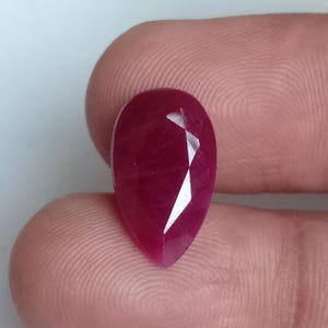 Puede incluir: Una piedra preciosa de color rojo intenso en forma de pera con facetas.