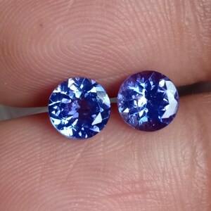 May include: Two round, faceted, blue gemstones. The gemstones are set in a bezel setting and have a high polish.
