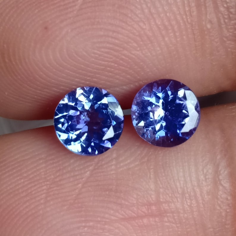 May include: Two round, faceted, blue gemstones. The gemstones are set in a bezel setting and have a high polish.
