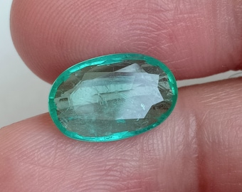 May include: A vibrant green oval emerald gemstone with a faceted cut. The emerald is set in a clear, smooth bezel.