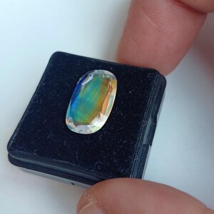 May include: A clear oval-shaped gemstone with iridescent rainbow colors, set in a black velvet display box.