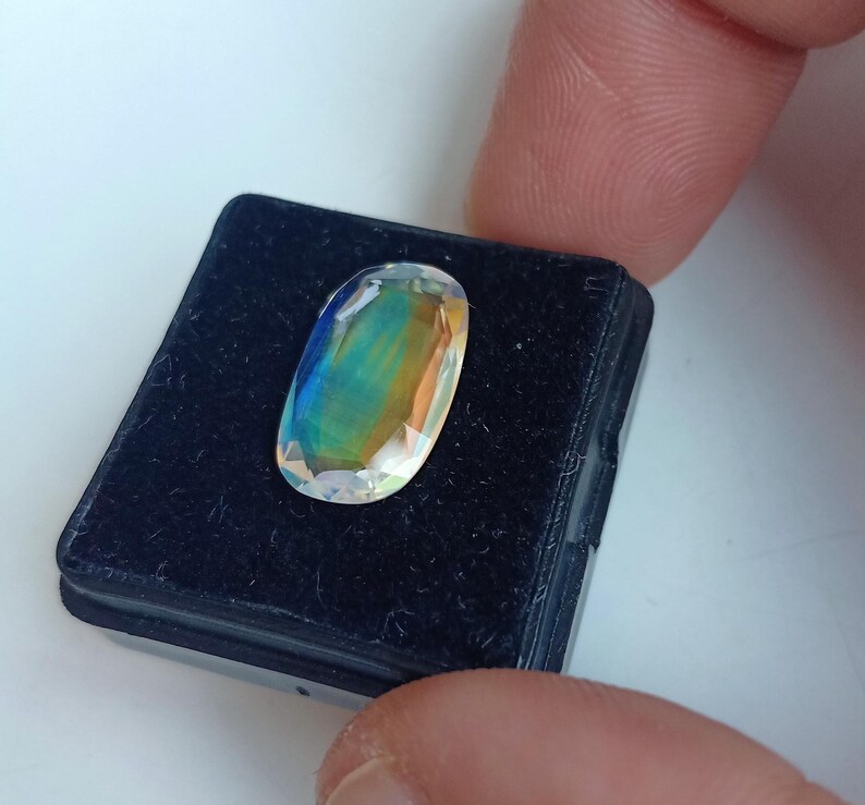 May include: A clear oval-shaped gemstone with iridescent rainbow colors, set in a black velvet display box.