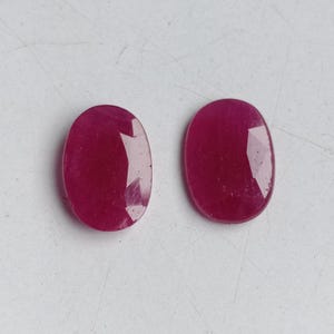 Könnte beinhalten: Zwei ovale, facettierte Edelsteine in einem tiefen Rosaton. Die Edelsteine sind glatt und poliert.