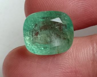 May include: A vibrant, emerald-cut gemstone with a rich green hue. The gem is held between fingers, showcasing its clarity and faceted surface. The cushion cut enhances the stone's brilliance, reflecting light. This gemstone is ideal for jewelry.