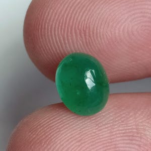May include: A bright green oval-shaped gemstone with a smooth, polished surface.