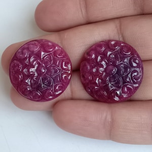 May include: Two round, pink and purple carved gemstone cabochons with a floral design.