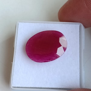 Puede incluir: Una piedra preciosa ovalada de color rojo intenso con un corte facetado, expuesta sobre un fondo blanco.