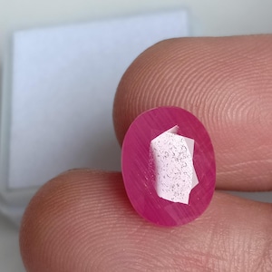 May include: A pink oval-shaped gemstone with a faceted design. The gemstone is set in a clear setting.