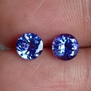 May include: Two round, faceted, blue gemstones. The gemstones are set in a clear, round setting.
