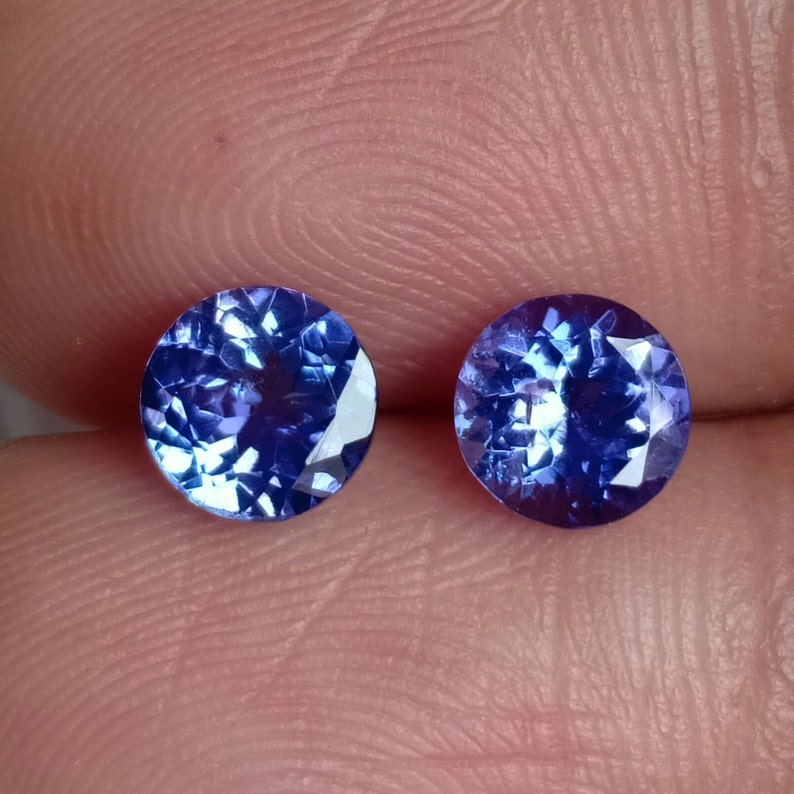 May include: Two round, faceted, blue gemstones. The gemstones are set in a clear, round setting.