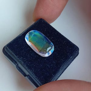 May include: A oval-shaped iridescent gemstone with blue, green, and purple hues, set in a black velvet display box.