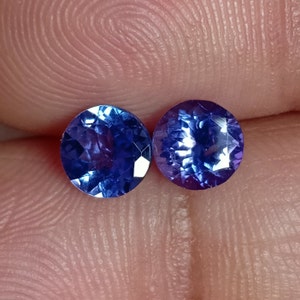 May include: Two round, faceted, blue gemstones. The gemstones are approximately 5mm in diameter.