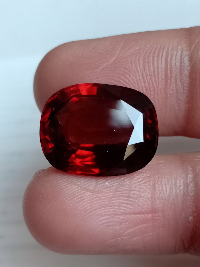 May include: A deep red gemstone with a faceted oval shape.