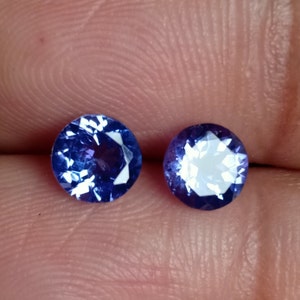 May include: Two round, faceted, purple gemstones with a white center.