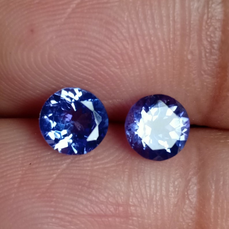 May include: Two round, faceted, purple gemstones with a white center.