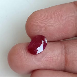 Op de afbeelding: Een ovaal geslepen, dieprode robijn edelsteen met een gefacetteerd oppervlak dat licht reflecteert. De steen vertoont een rijke, verzadigde karmozijnrode tint met zichtbare interne helderheid en scherpe, geometrische facetten op de bovenkant.