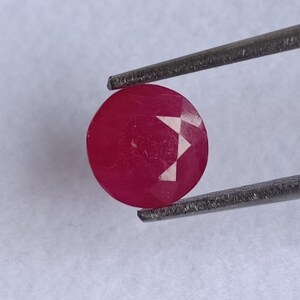 Könnte beinhalten: Ein leuchtend rosa ovaler Edelstein mit facettiertem Schliff, gehalten von einer Pinzette.