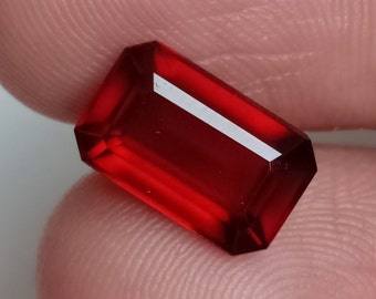 May include: A deep red, faceted gemstone with a rectangular shape.