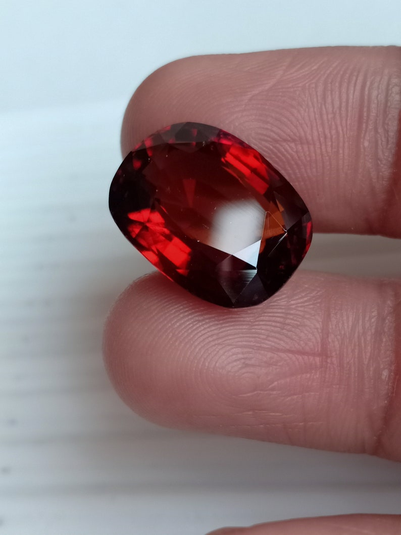 May include: A deep red gemstone with a faceted cut. The gemstone is oval shaped and has a high polish.