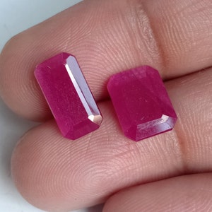 May include: Two pink rectangular gemstones with a faceted cut.