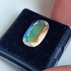May include: A clear oval-shaped gemstone with iridescent colors, including green, blue, and orange, displayed in a black velvet box.