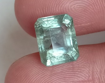 May include: A light green emerald gemstone cut in a square shape with bevelled edges.